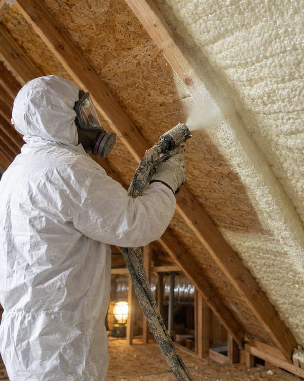 A technician spraying foam insulation onto the underside of a roof deck